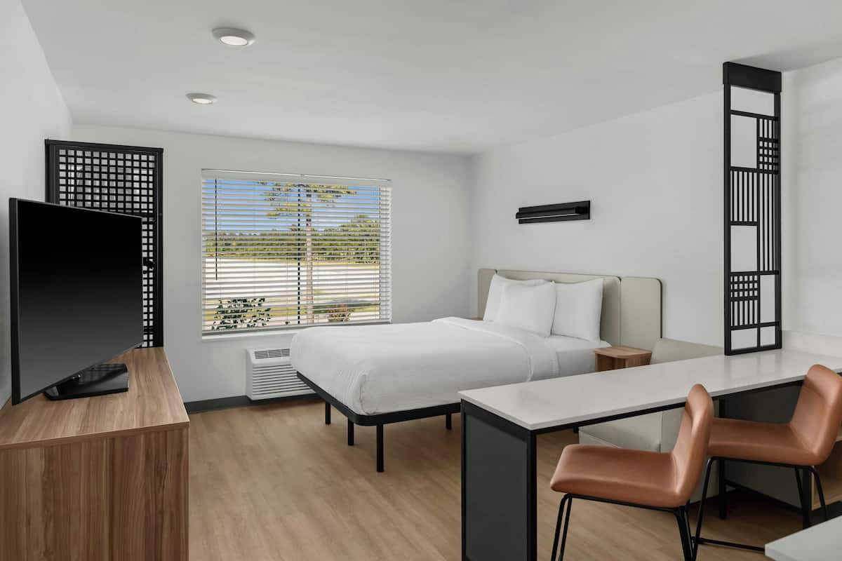 Una habitación de hotel moderna con cama, escritorio, televisor y zona de estar.