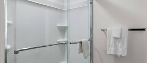 Ducha con paredes de vidrio, una barra para toallas y una toalla blanca.