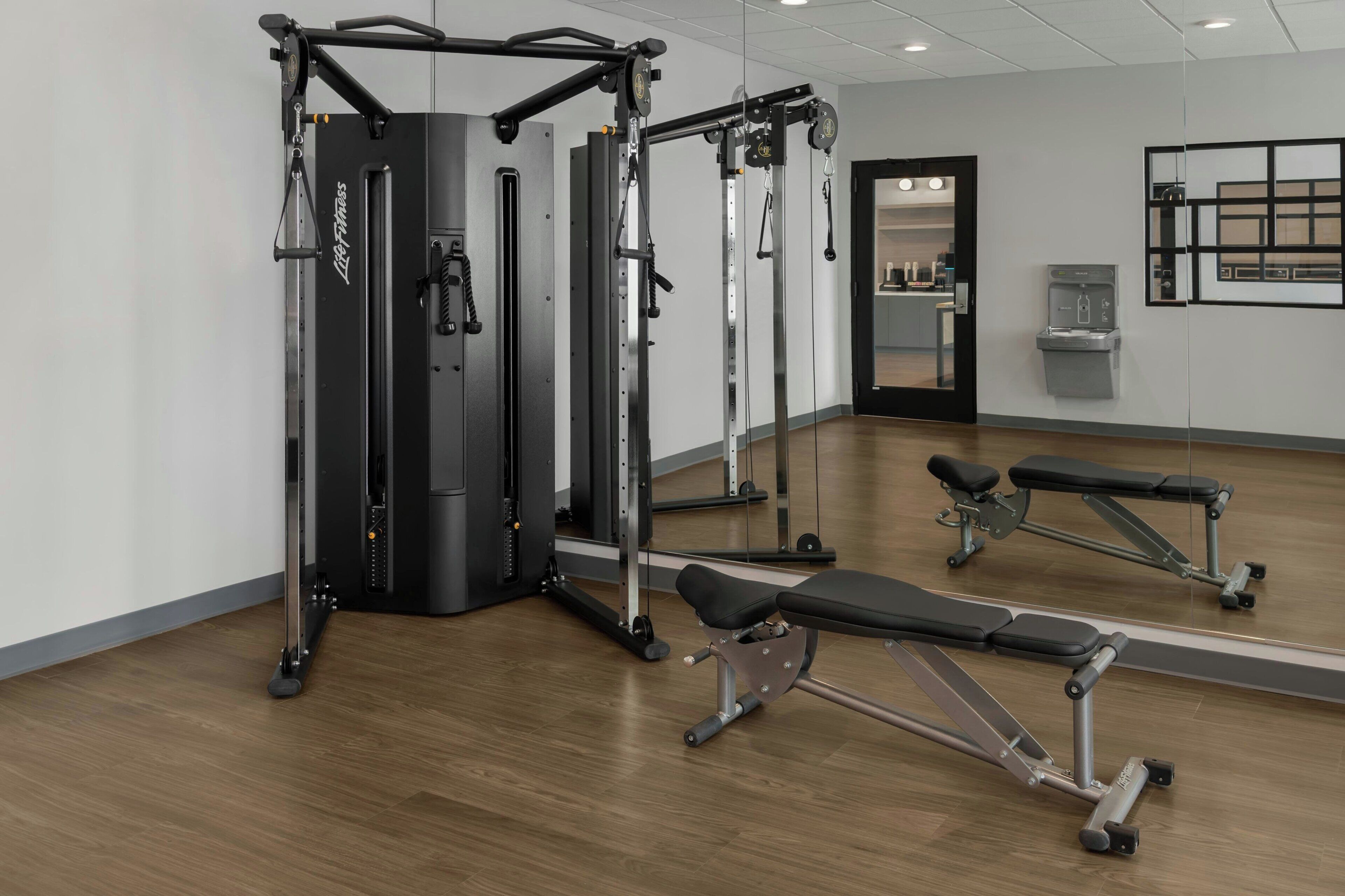 A gym with weightlifting equipment, benches, and a mirrored wall.