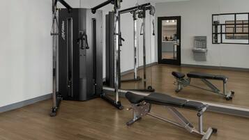 A gym with weightlifting equipment, benches, and a mirrored wall.