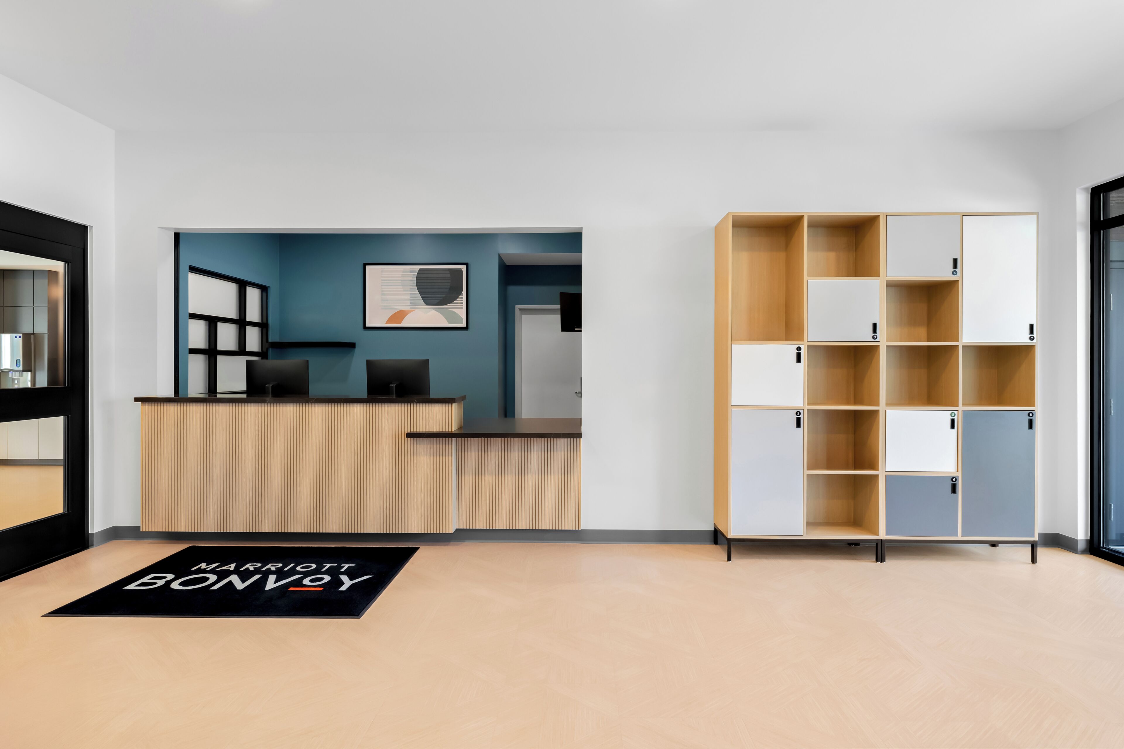 A hotel reception area with a wooden reception desk, a blue wall with artwork, and a storage unit with multiple compartments.