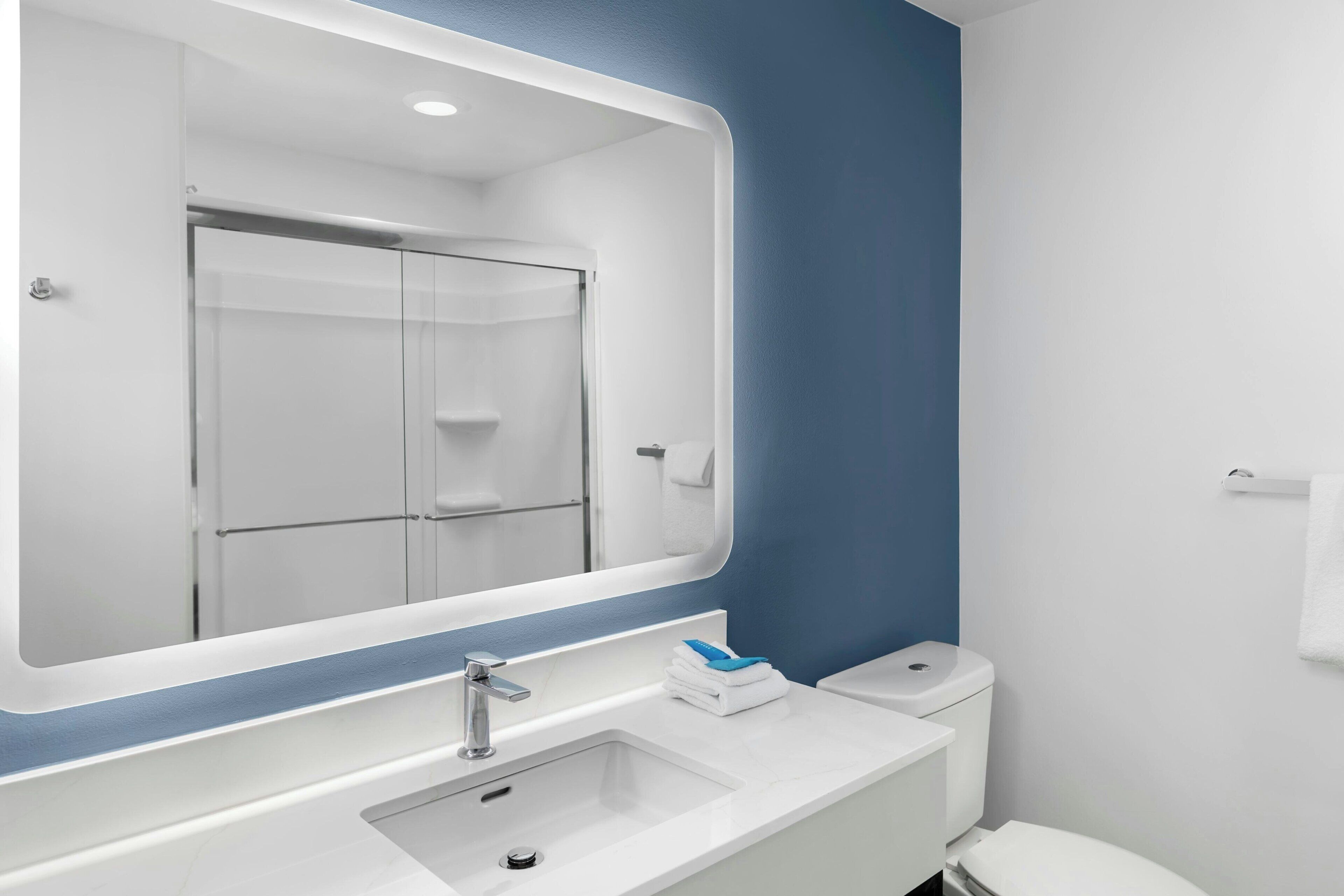 A modern bathroom with a large mirror, a sink, a toilet, and a shower.