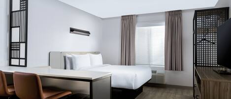 A hotel room with a bed, desk, chairs, and a TV.