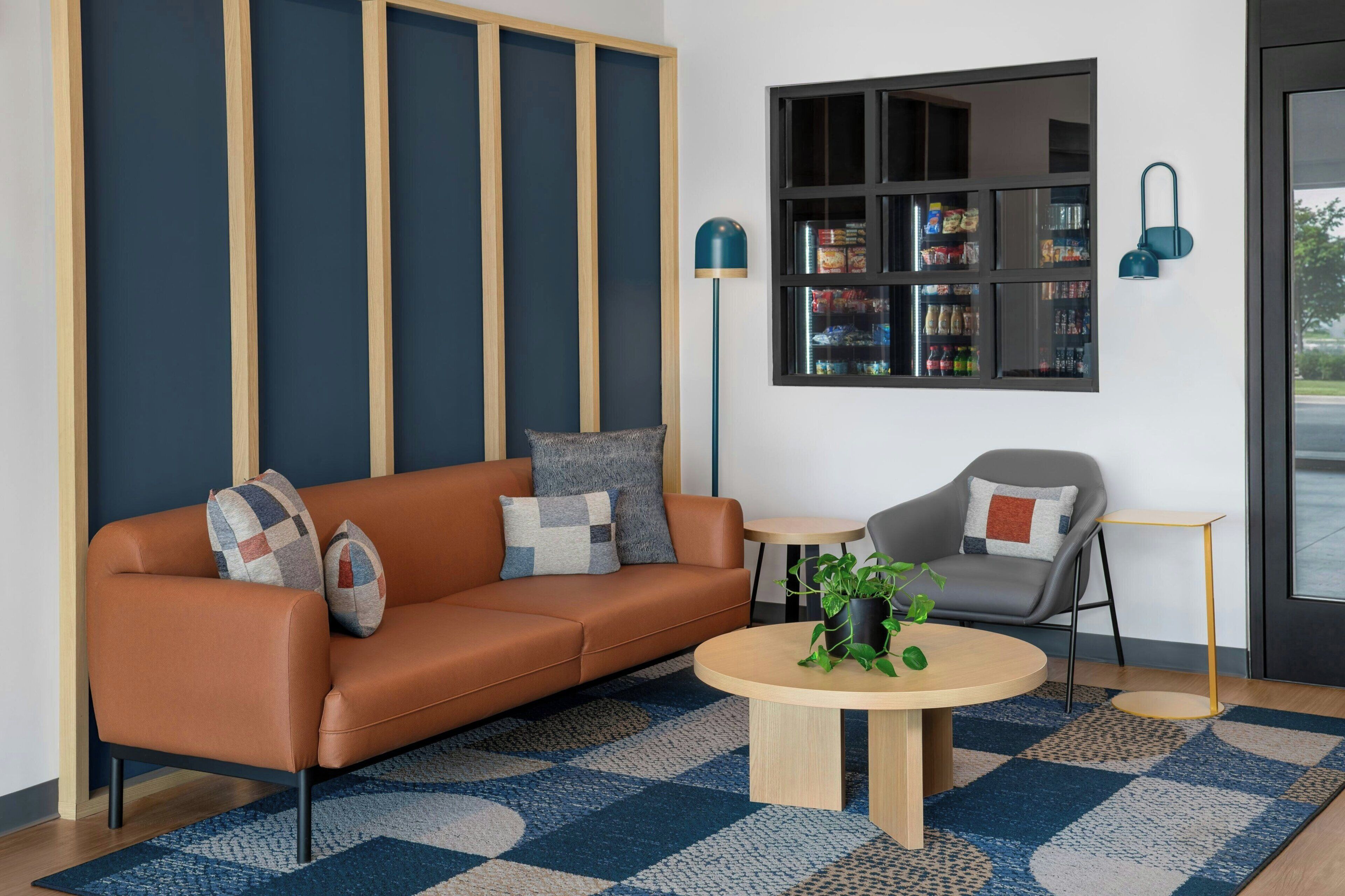 Ein modernes Wohnzimmer mit einem Ledersofa, einem runden Couchtisch, einem grauen Sessel, einem Bücherregal und einer Stehlampe.