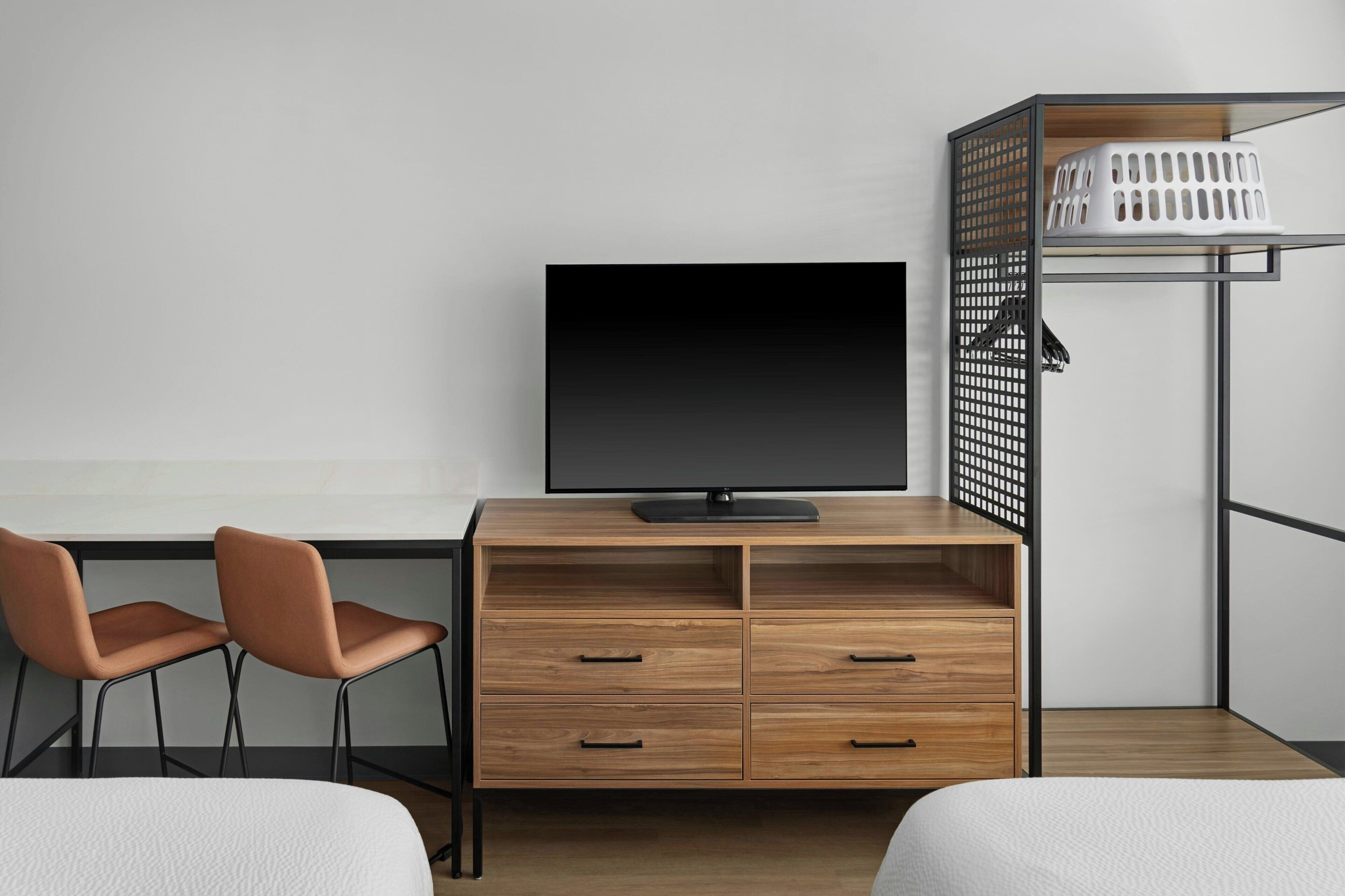 A modern room with a wooden desk, two chairs, a television, a wardrobe, and a bed.