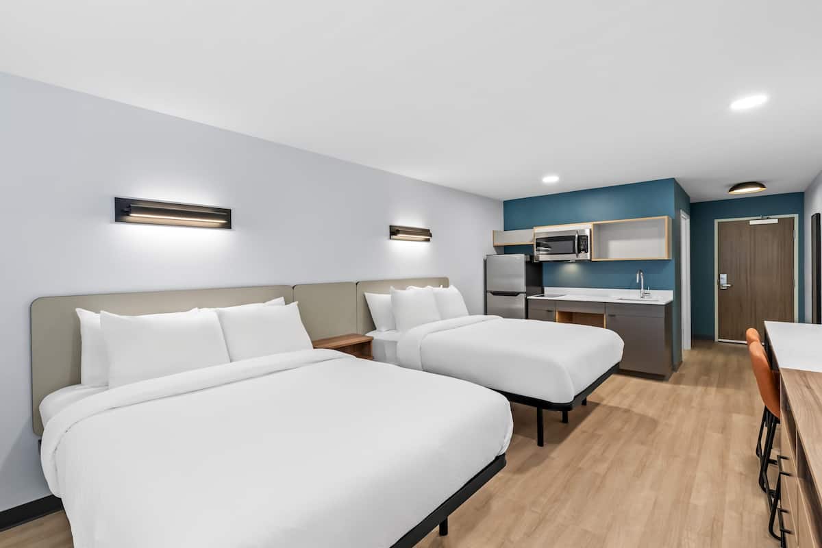 Een hotelkamer met twee bedden, een kitchenette en een eethoek.