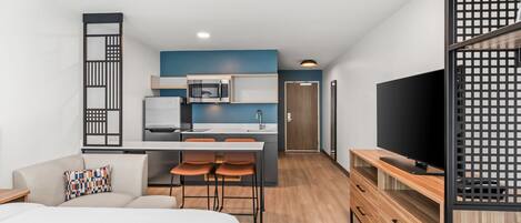 A modern hotel room with a kitchenette, a bed, a TV, and a dining area.