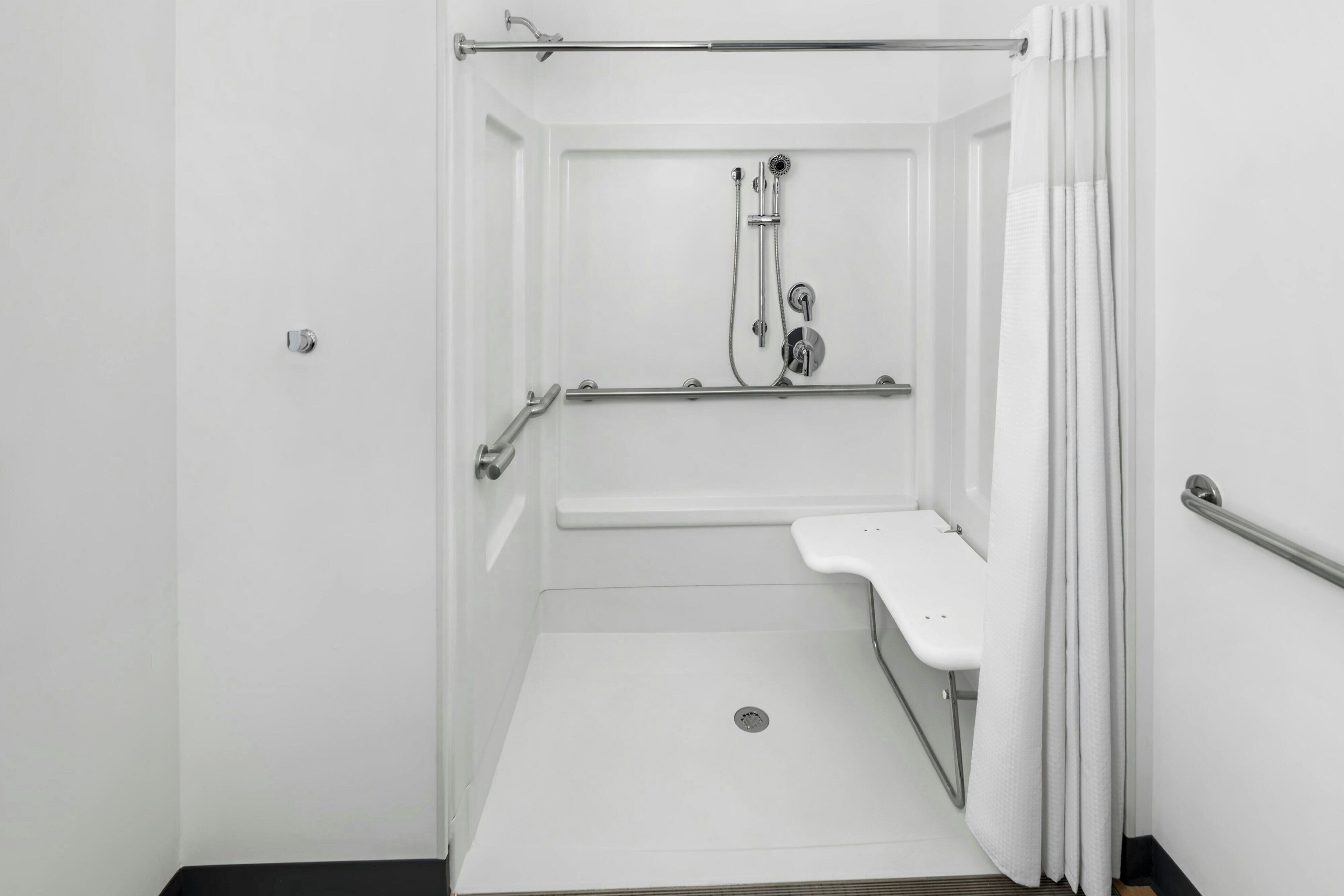 A white, accessible shower room with a grab bar, a handheld showerhead, and a handheld faucet.