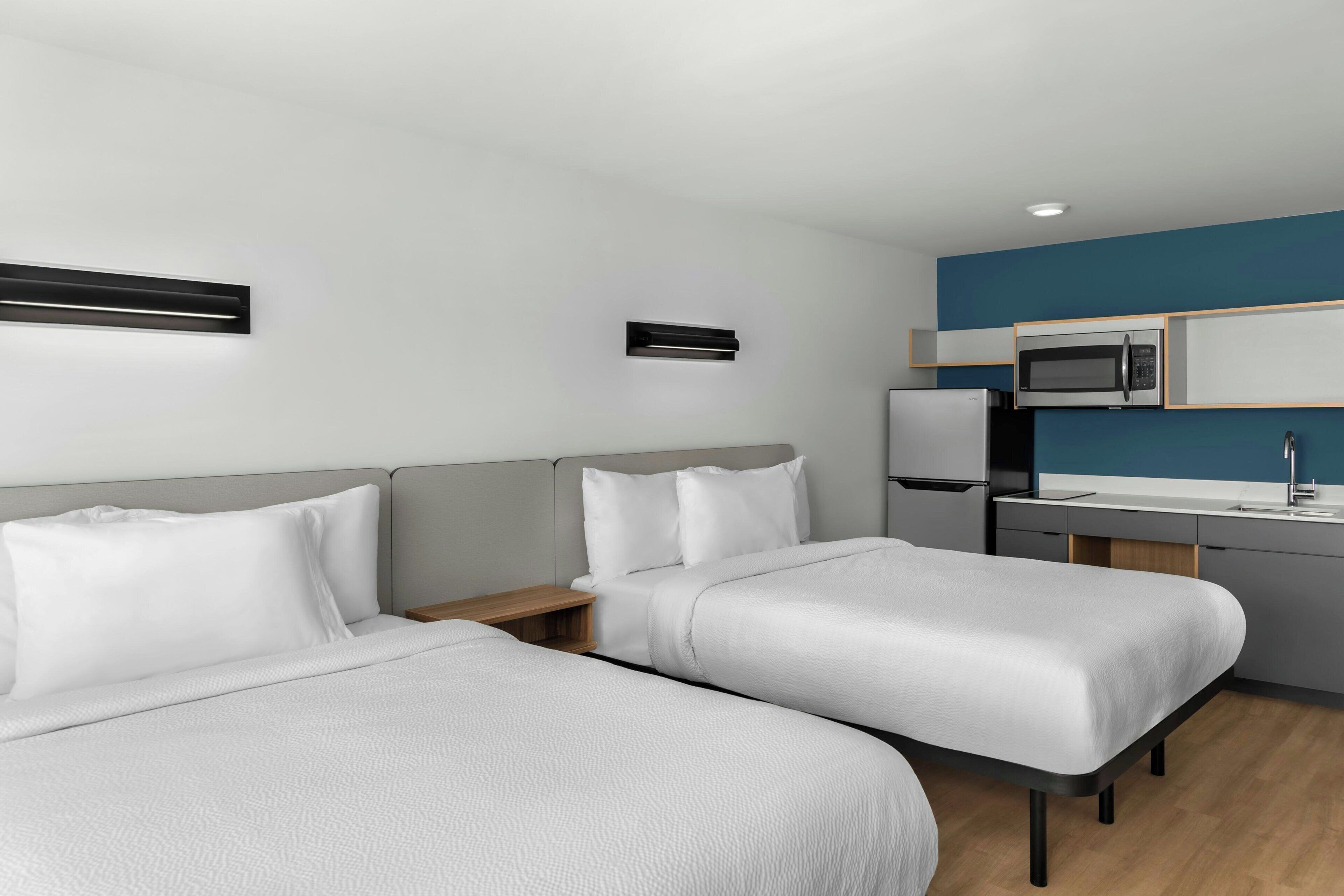 A hotel room with two beds, a kitchenette with a microwave, refrigerator, and sink.