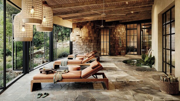 Un salón luminoso con suelo de piedra, vigas de madera en el techo y grandes ventanales con vistas al exterior.