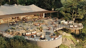 Un amplio espacio al aire libre con diversas opciones de asientos, un hogar central y una zona cubierta con mesas y sillas.