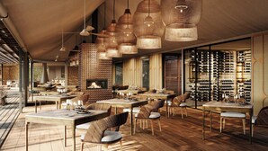 Un restaurante con suelo de madera, sillas de mimbre y lámparas colgantes de mimbre. Las mesas están preparadas con copas de vino y platos.