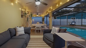 Un'area patio all'aperto con piscina, ventilatori a soffitto, luci decorative e un tavolo da pranzo con sedie.