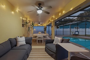 An outdoor patio area with a pool, ceiling fans, string lights, and a dining table with chairs. - Sip of Sun (New Smyrna Beach)
