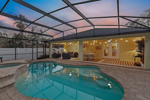 A covered outdoor swimming pool with a patio area, seating, and a view of the sky. - Sip of Sun (New Smyrna Beach)