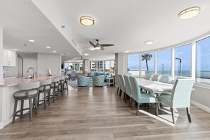 A spacious kitchen with a long counter, bar stools, and a dining area with a high table and chairs. - Peck Plaza 9NW (Daytona Beach Shores)