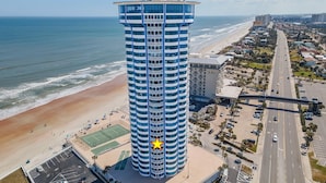 Ein Hochhaus-Hotel mit einer markanten blau-weißen Fassade, gelegen neben einem Strand und einer belebten Straße.