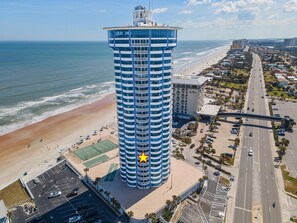 A high-rise hotel with a distinctive blue and white facade, located adjacent to a beach and a busy road. - Peck Plaza 9NW (Daytona Beach Shores)
