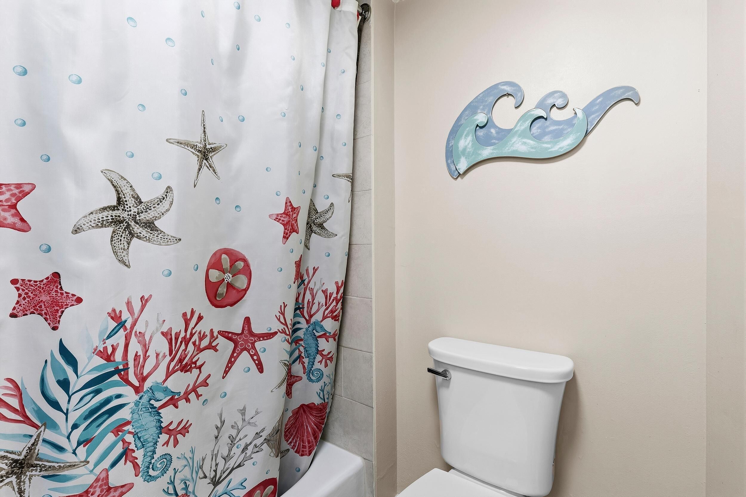 A bathroom with a white toilet, a shower curtain with sea-themed designs, and a wall-mounted seahorse decoration.
