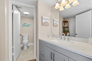 A bathroom with a toilet, a sink, and a mirror. - Peck Plaza 9NW (Daytona Beach Shores)