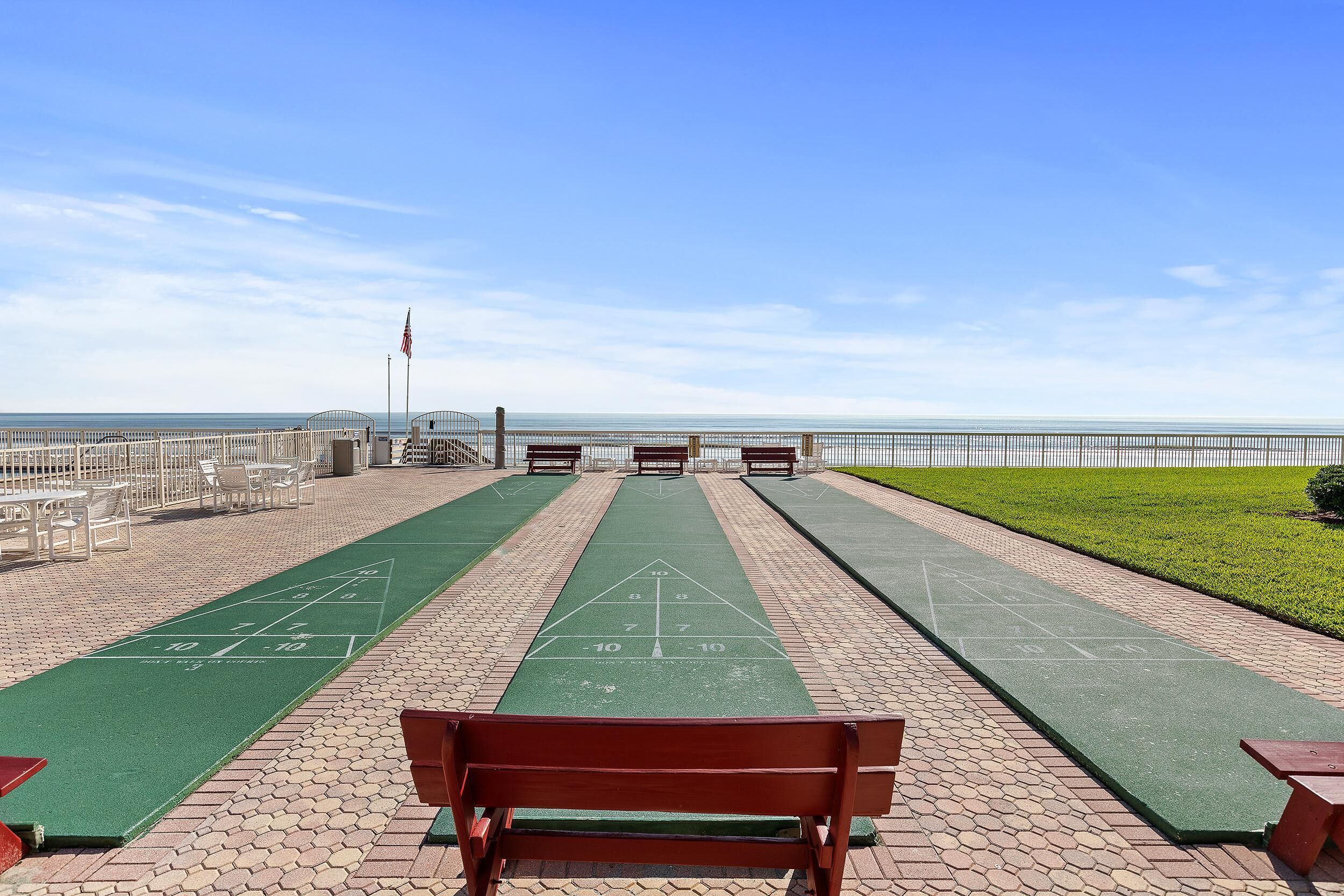 A park with a green shuffleboard court, a wooden bench, and a view of the ocean.