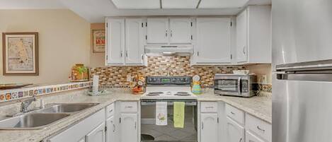Una cocina con armarios blancos, estufa, microondas y refrigerador.