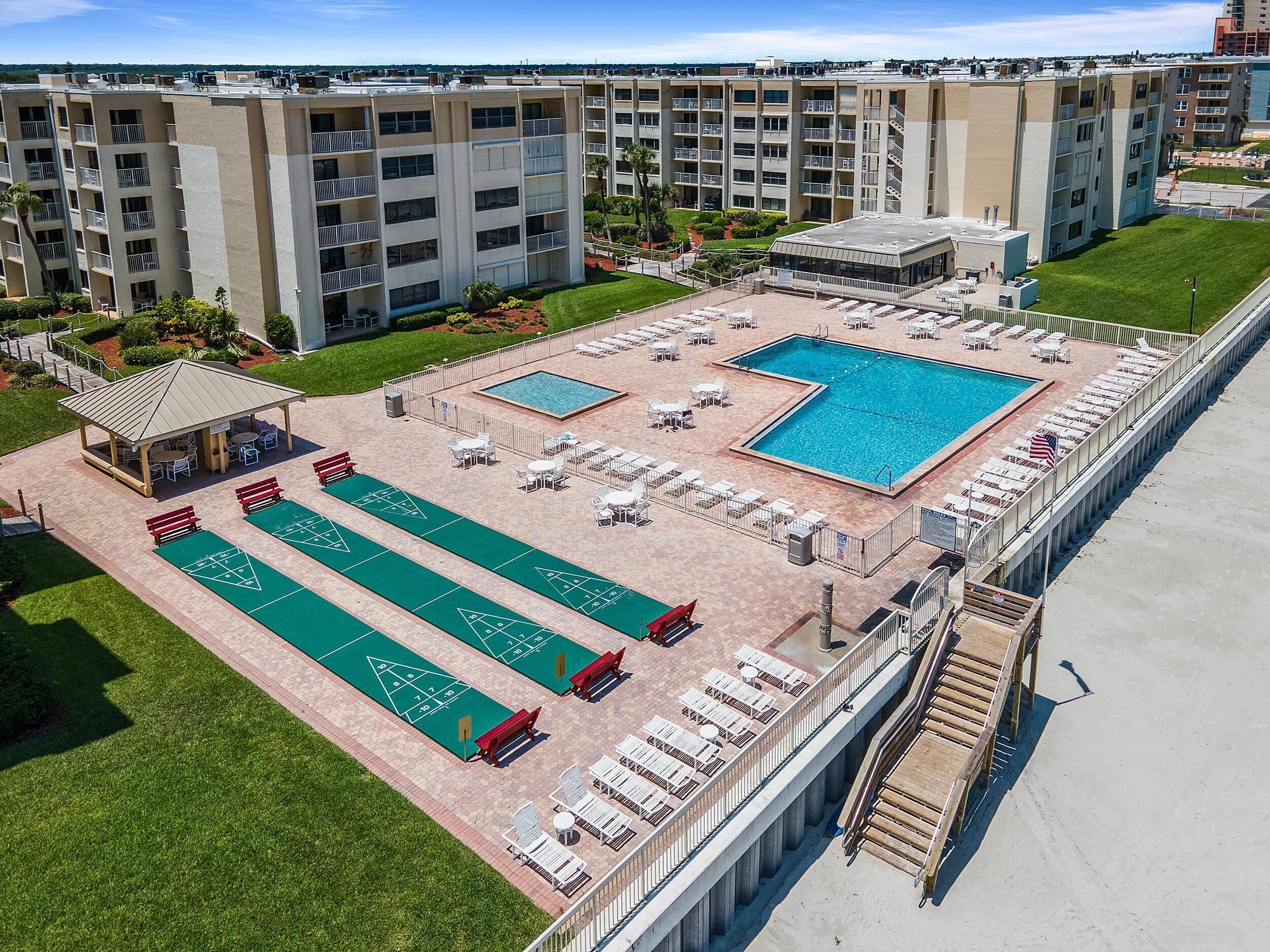 A rooftop pool area with multiple pools, shuffleboard courts, and lounge chairs.