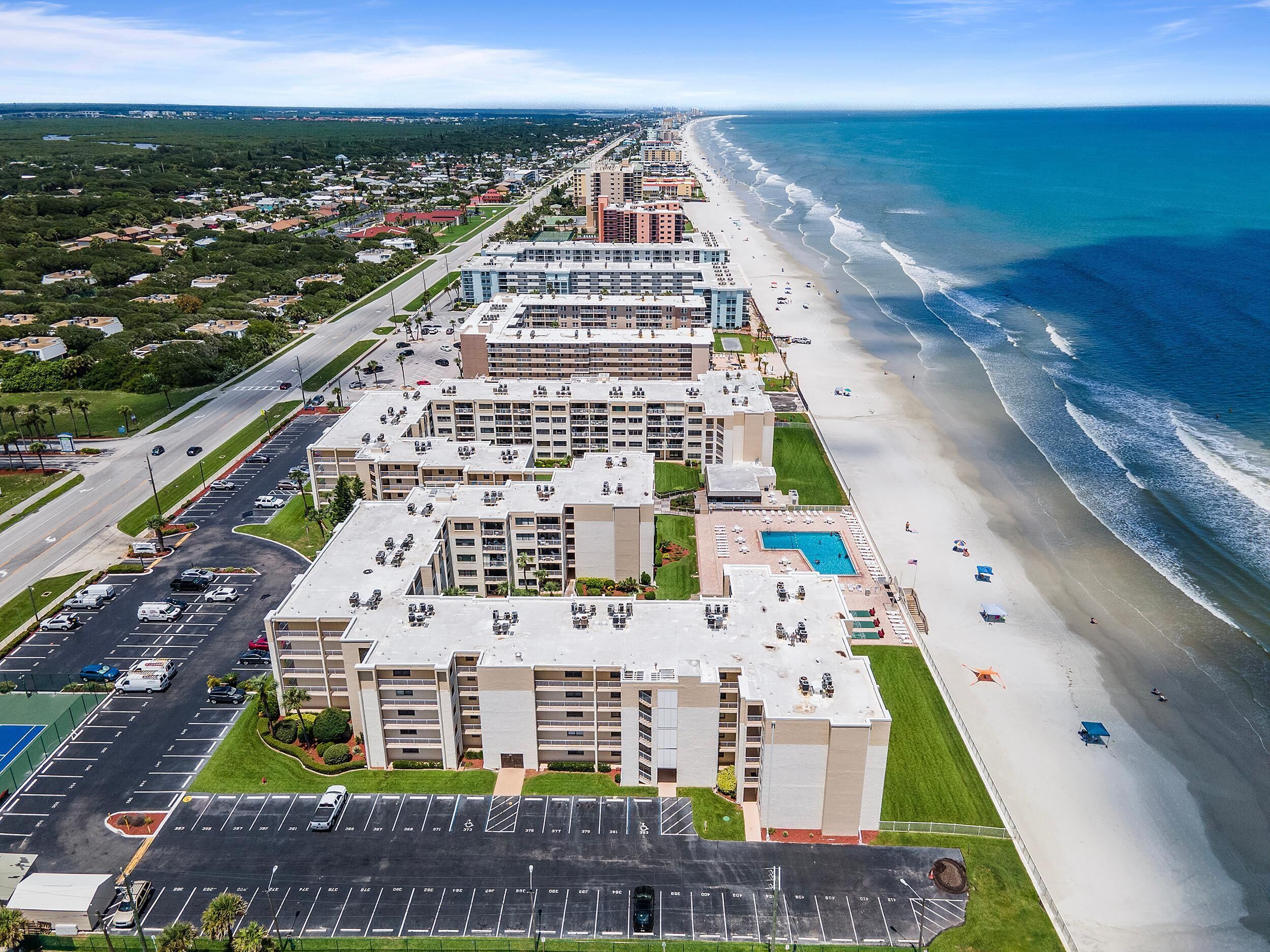 Un hotel frente a la playa con varias edificaciones, estacionamiento y acceso directo a la playa.