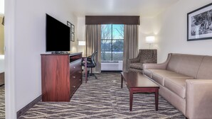 A hotel room with a TV, a desk, a sofa, and a patterned carpet. - Cobblestone Hotel & Suites - Monte Vista (Monte Vista)