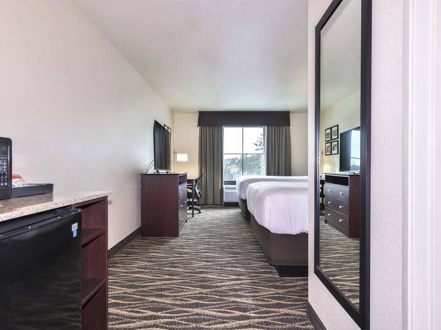 A hotel room with a kitchenette, a bed, a desk, a chair, a mirror, and a window with curtains.