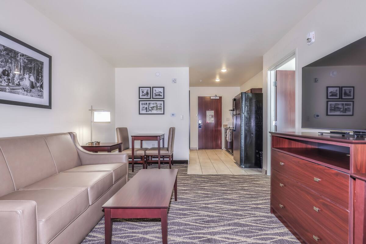 Una sala moderna con sofá, mesa de centro y mesa de comedor. Hay una zona de cocina con refrigerador y televisor.