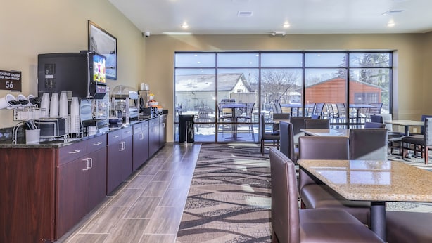 A modern breakfast lounge with a coffee machine, seating area, and large windows offering a view of the outside. - Cobblestone Hotel & Suites - Monte Vista (Monte Vista)