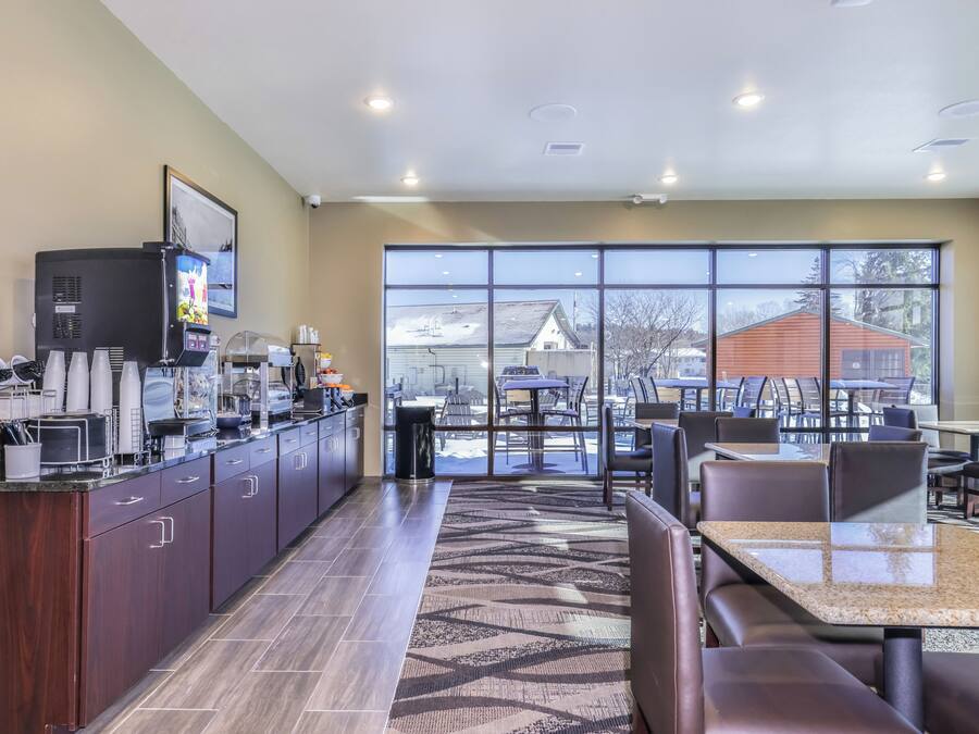 A modern breakfast lounge with a coffee machine, seating area, and large windows offering a view of the outside.