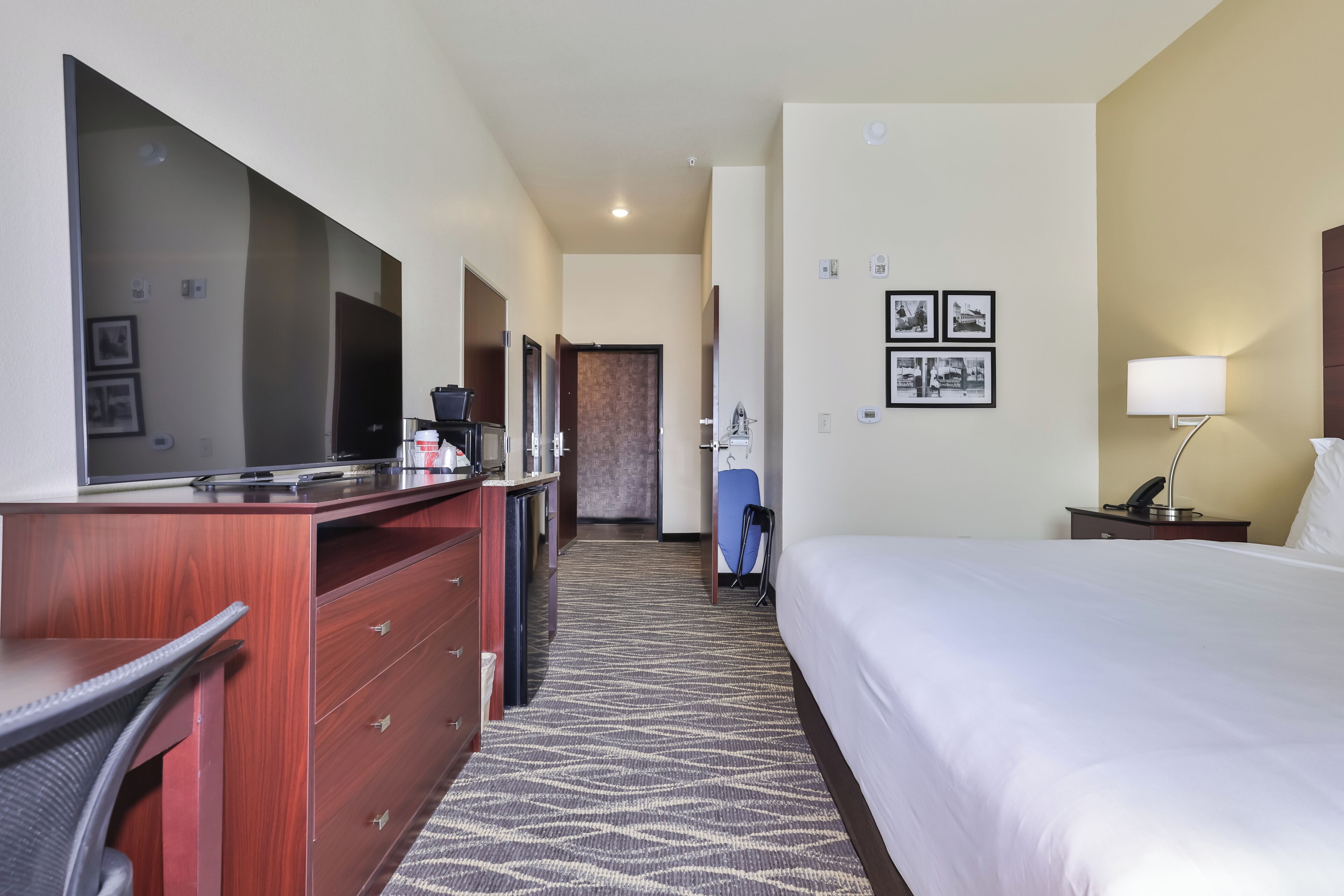 A hotel room with a bed, a desk with a chair, a dresser, a television, a lamp, and a wall-mounted telephone.