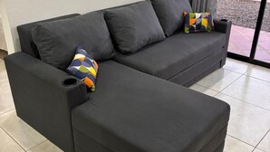 Ein dunkelgraues Sofa mit farbenfrohem geometrischem Kissen und einer schwarzen Armlehne.