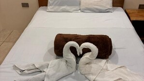 Ein Bett mit weißen Leinen, einer braunen Decke und zwei Handtüchern, die in Herzform drapiert sind.