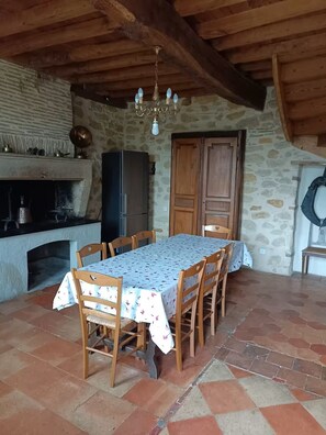 A rustic dining area with a stone wall, wooden ceiling beams, a chandelier, a table with chairs, and a fireplace. - Le Cœur des Vignes. Family gite located in the heart of our family estate (Verdelais)