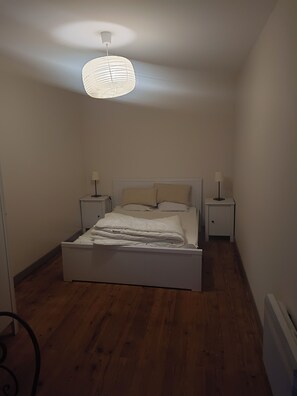 A bedroom with a bed, two bedside tables, a hanging light fixture, and a radiator. - Le Cœur des Vignes. Family gite located in the heart of our family estate (Verdelais)