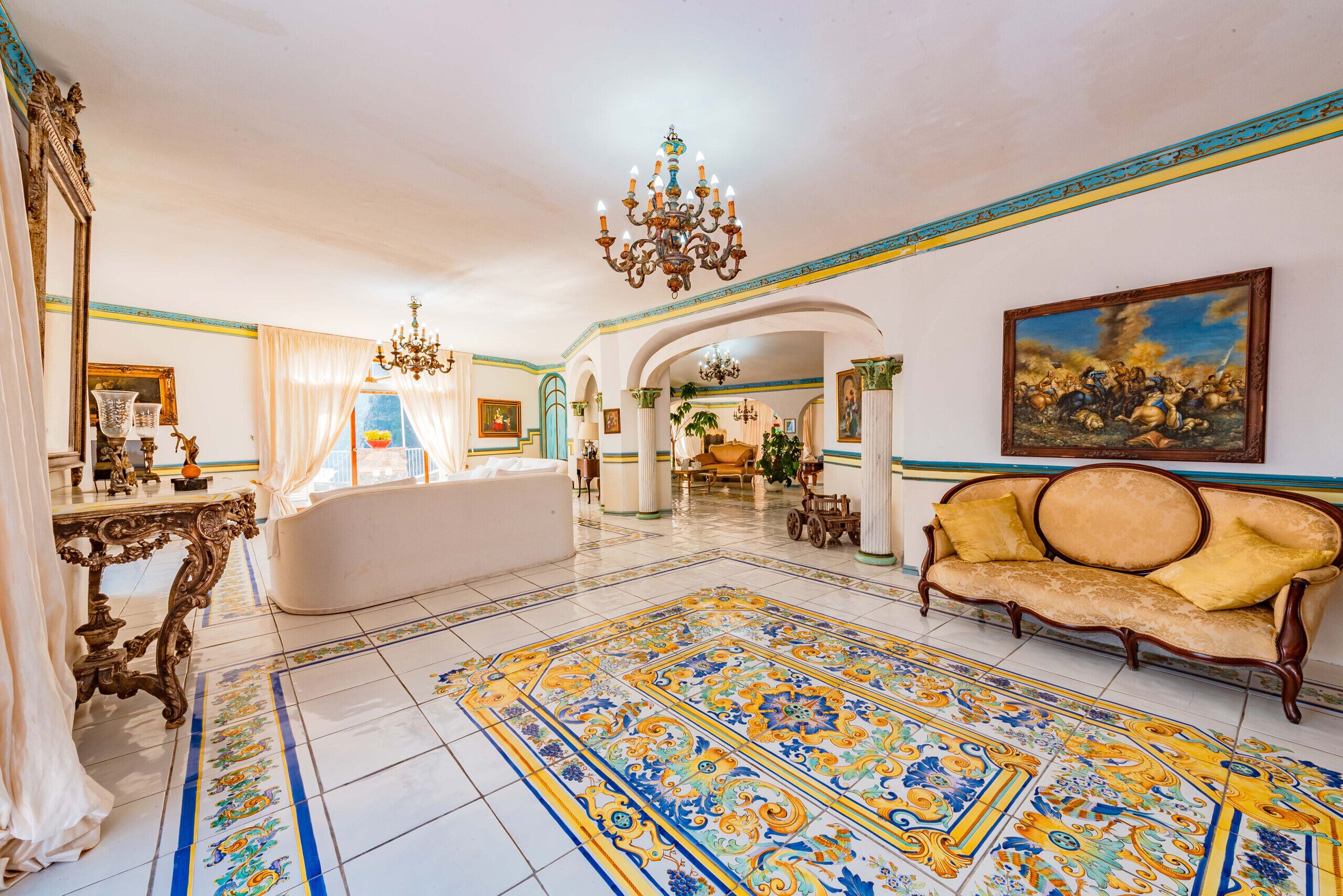 A spacious living room with a large ornate chandelier, a sofa, and a patterned rug.