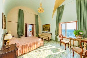 Una habitación con cama, sofá, mesa de comedor con sillas, candelabro y vista al mar.