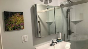 Ein Badezimmer mit einem weißen Waschbecken, einer Glasdusche und einem wandmontierten Spiegel.