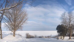 Eine verschneite Landschaft mit einem zugefrorenen See, kahlen Bäumen und einem klaren Himmel.