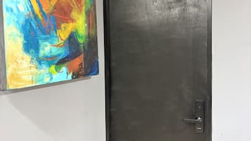 Una puerta con una placa de número, una puerta negra y un cuadro abstracto de colores en la pared.