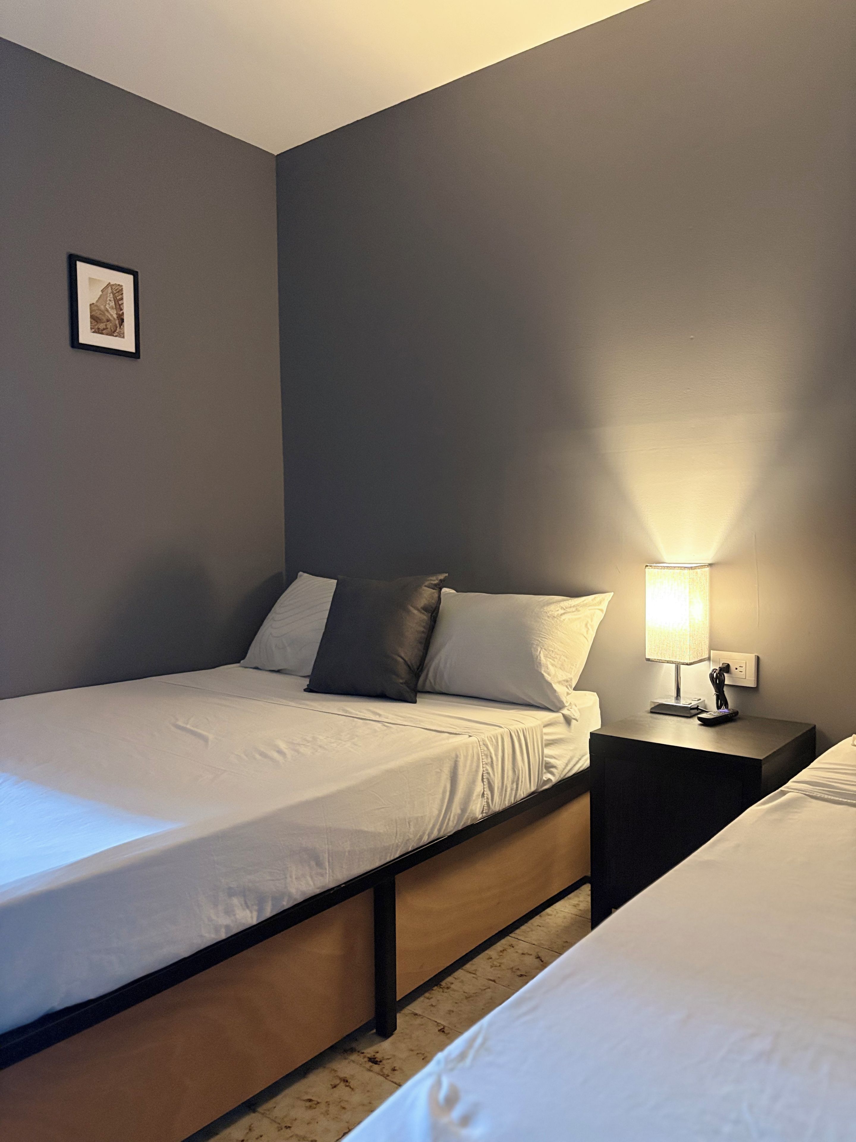 Ein Einzelbett mit Holzrahmen, ein Nachttisch mit Lampe und ein gerahmtes Bild an der Wand.