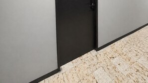 A closed black door with a handle, a light grey wall, and a tiled floor. - Adhoc Macro (Monterrey)