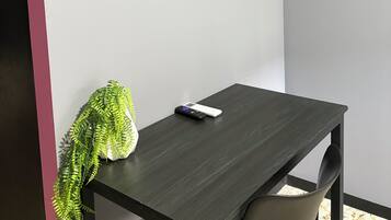 Una habitación con televisión de pantalla plana montada en la pared, una mesa de madera oscura, una silla y una planta en maceta.