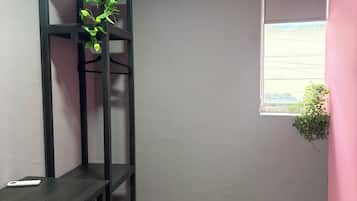 Una habitación con un escritorio, una estantería negra, un aire acondicionado, una ventana y una planta.