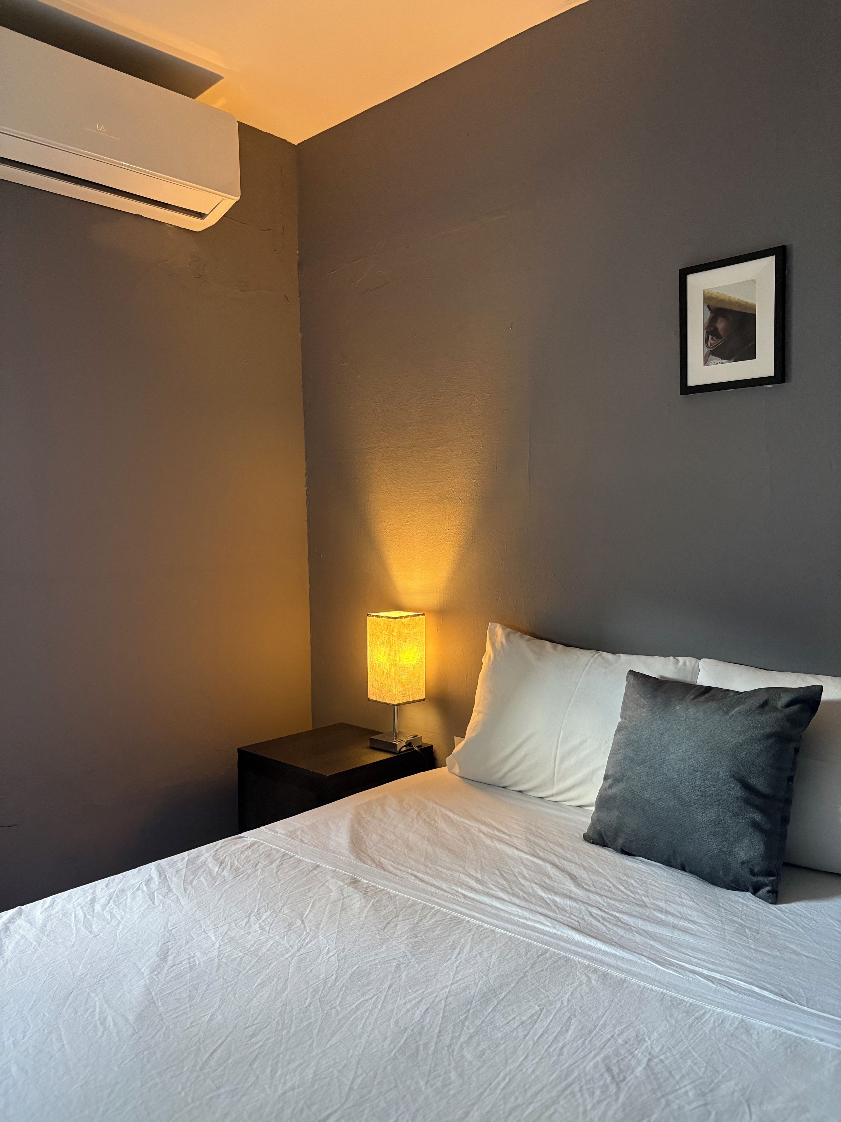 Une chambre d’hôtel équipée d’un lit, d’une table de chevet, d’une lampe et d’un appareil de climatisation.