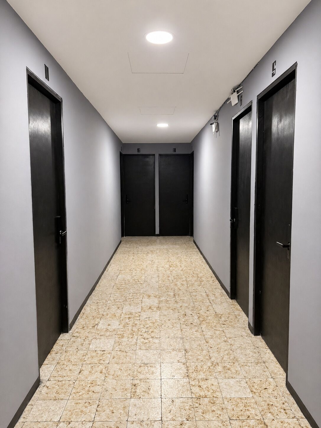 Un pasillo con dos puertas, piso de baldosas y una lámpara en el techo.