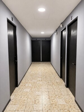 Un couloir avec deux portes, un sol carrelé et un luminaire au plafond.